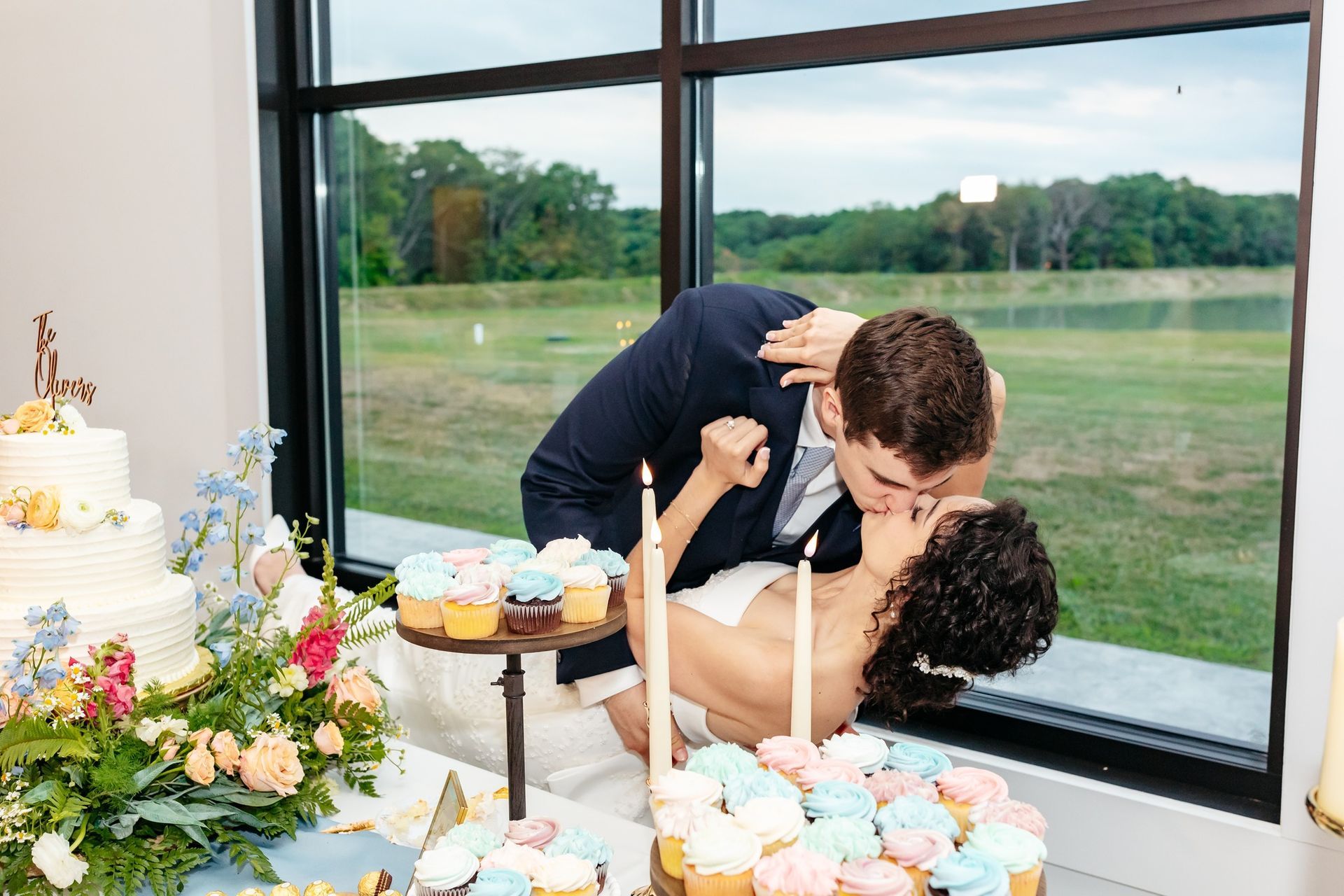 bride and groom kissing behind cake and cupcake table
