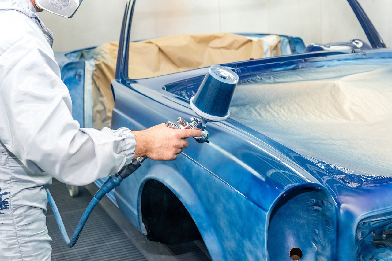 A man is spray painting a blue car in a garage.
