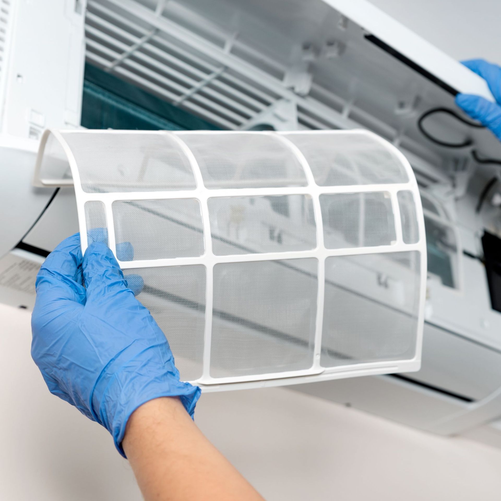 CC Air Services LLC - A person wearing blue gloves is holding a filter in front of an air conditioner.