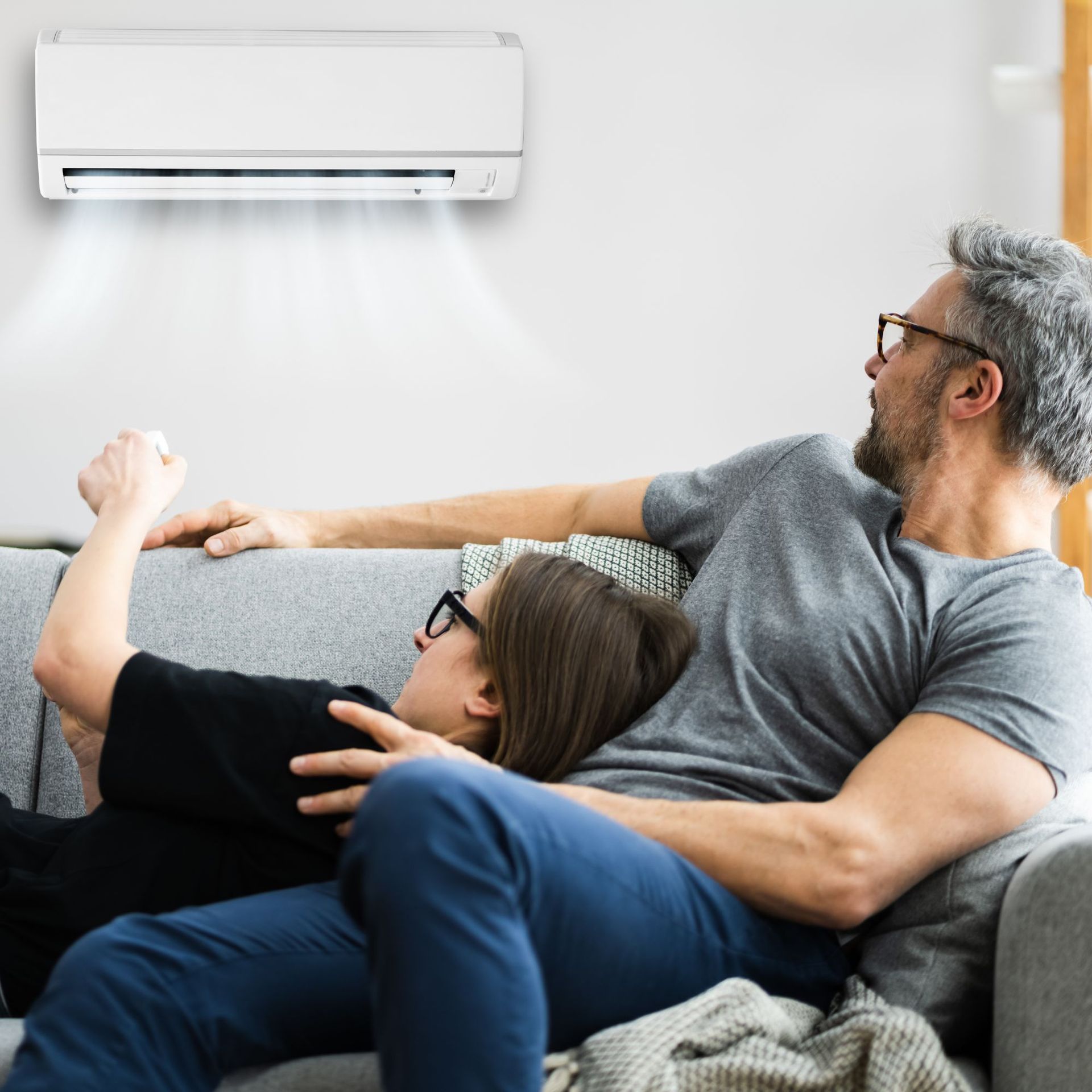 CC Air Services LLC - A man and a woman are sitting on a couch under an air conditioner.