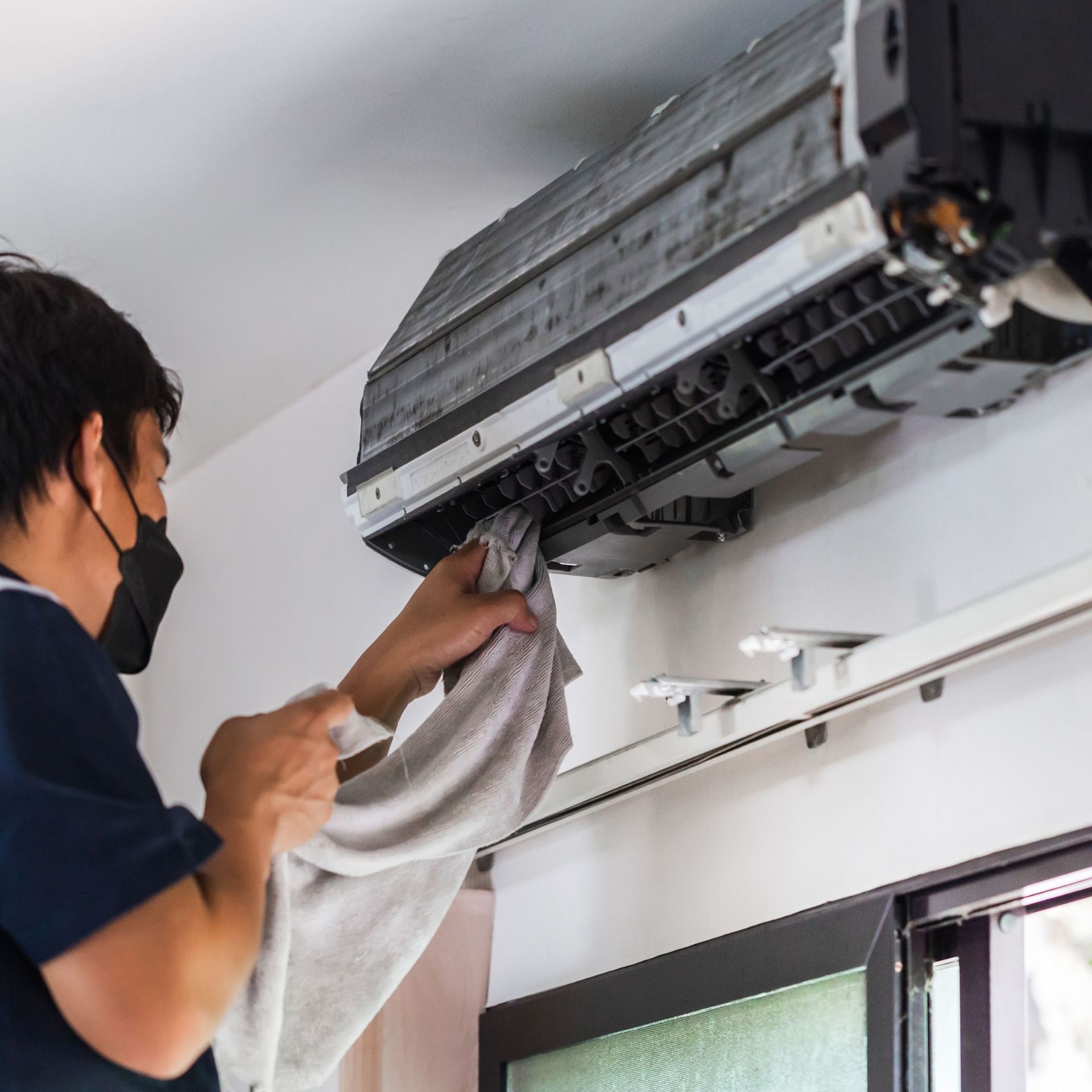 CC Air Services LLC - A man wearing a mask is cleaning an air conditioner with a towel