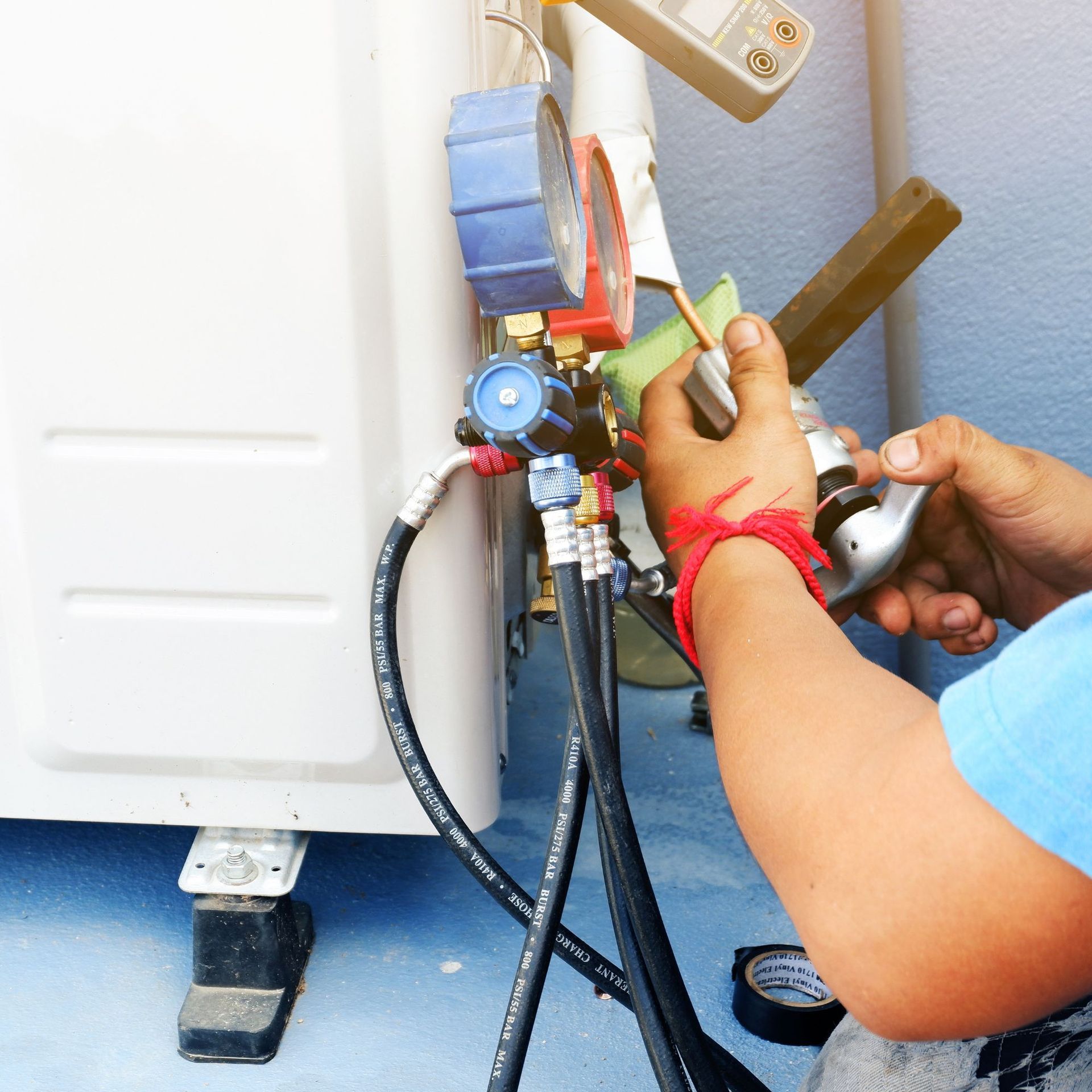 CC Air Services LLC - A man is working on an air conditioner with a gauge attached to it