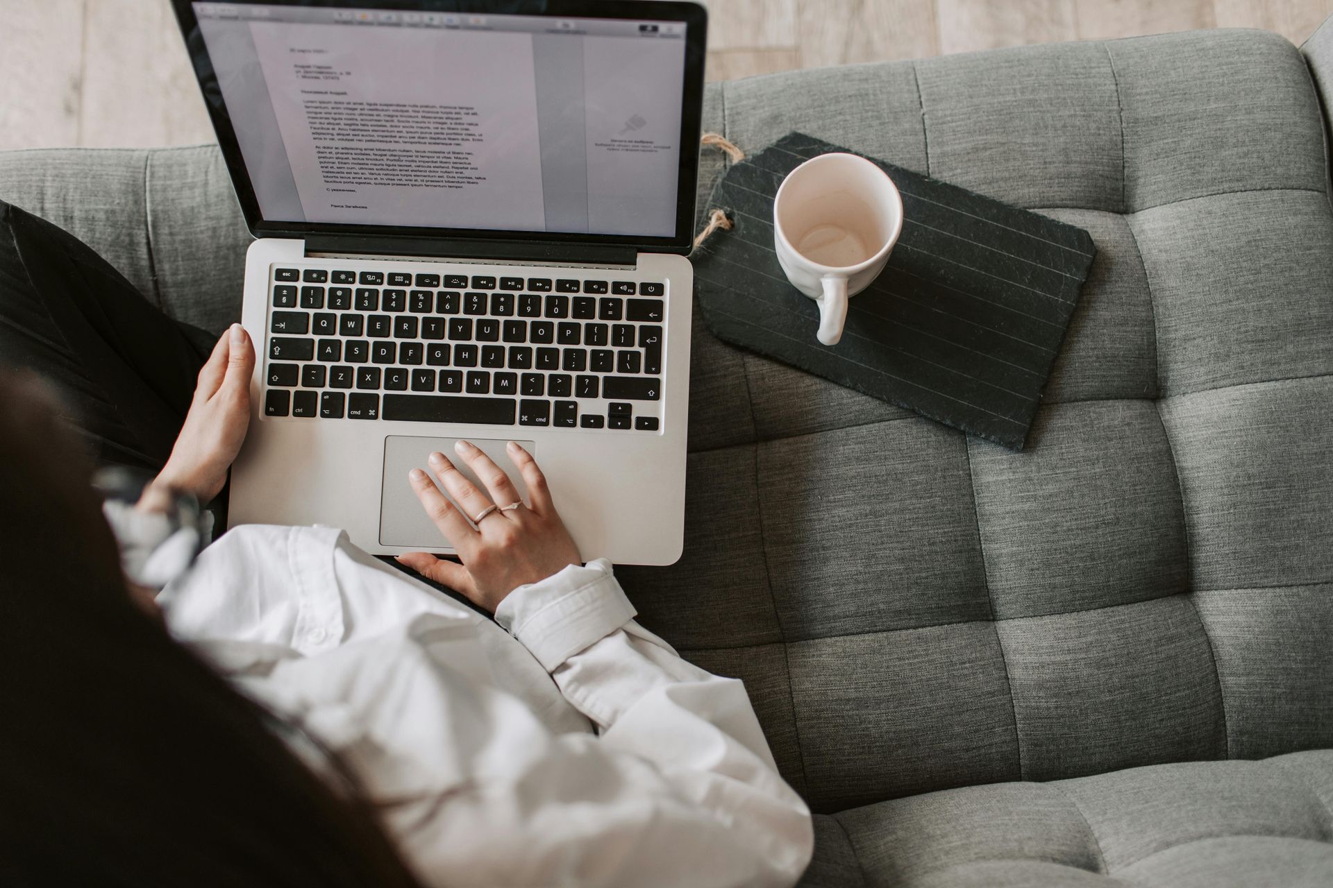 Person using a laptop on a couch with a mug and small tray.