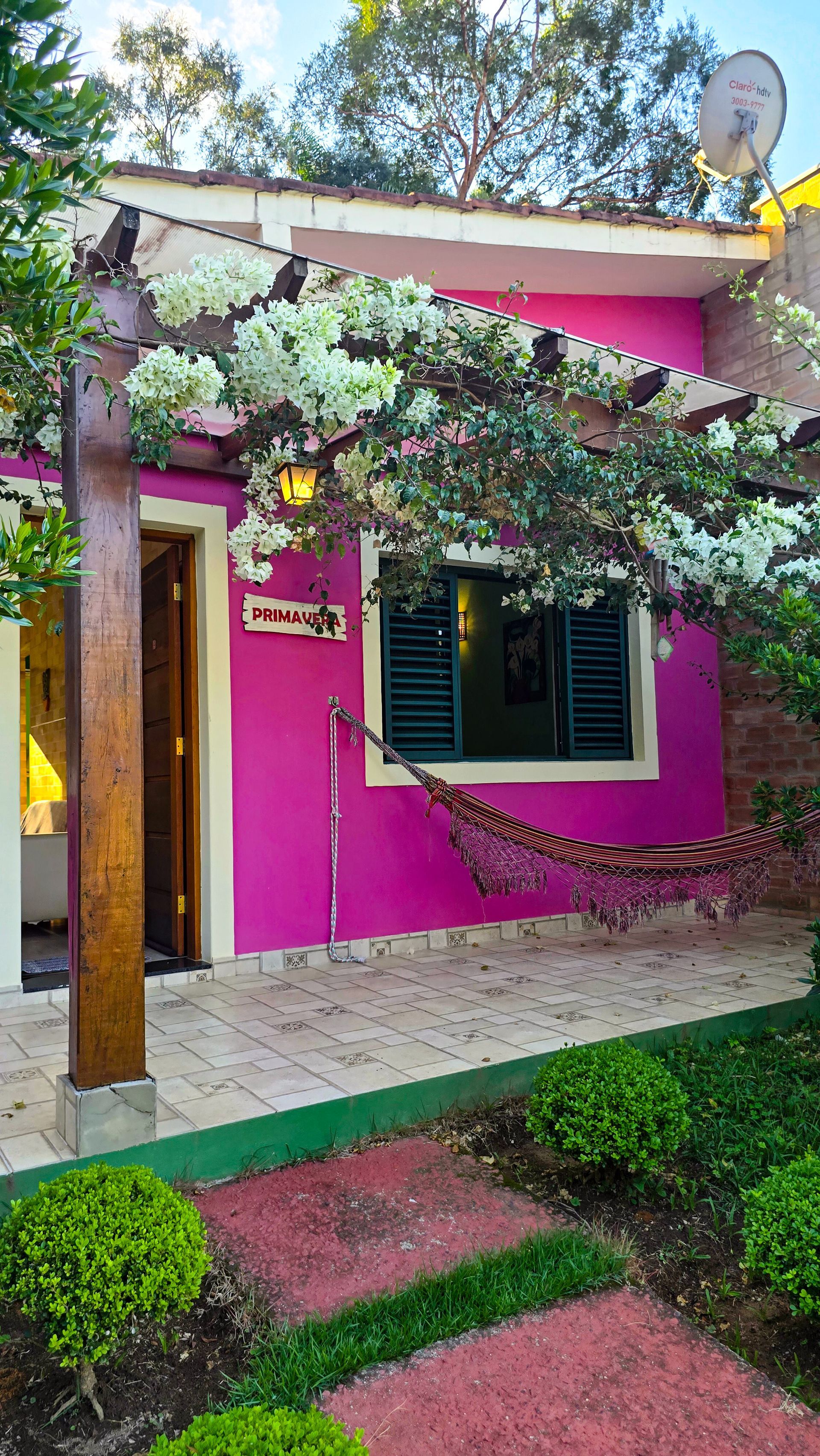 Casa rosa com flores brancas e uma rede.