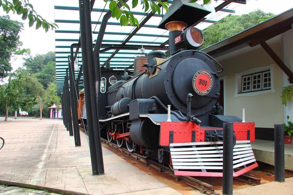Trem a vapor preto e vermelho sobre trilhos sob uma passarela coberta.