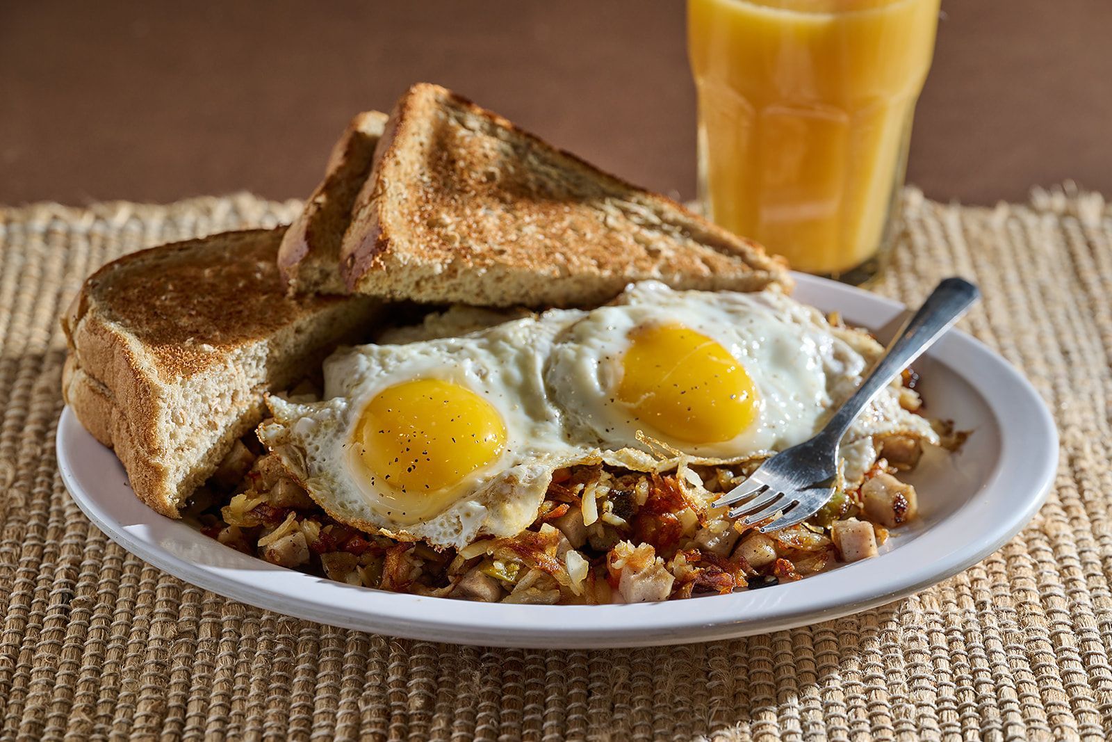 A breakfast plate with two sunny-side up eggs, hash browns, and two slices of toast, with a glass of orange juice.