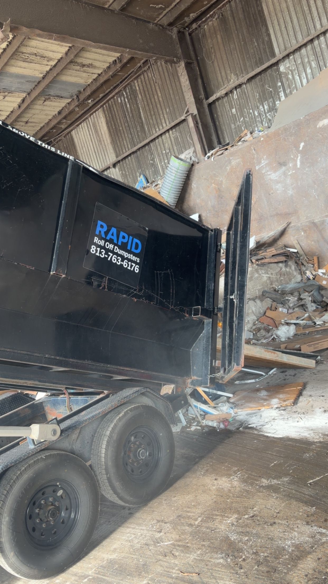 Three green dumpsters overflowing with cardboard and trash on a city sidewalk