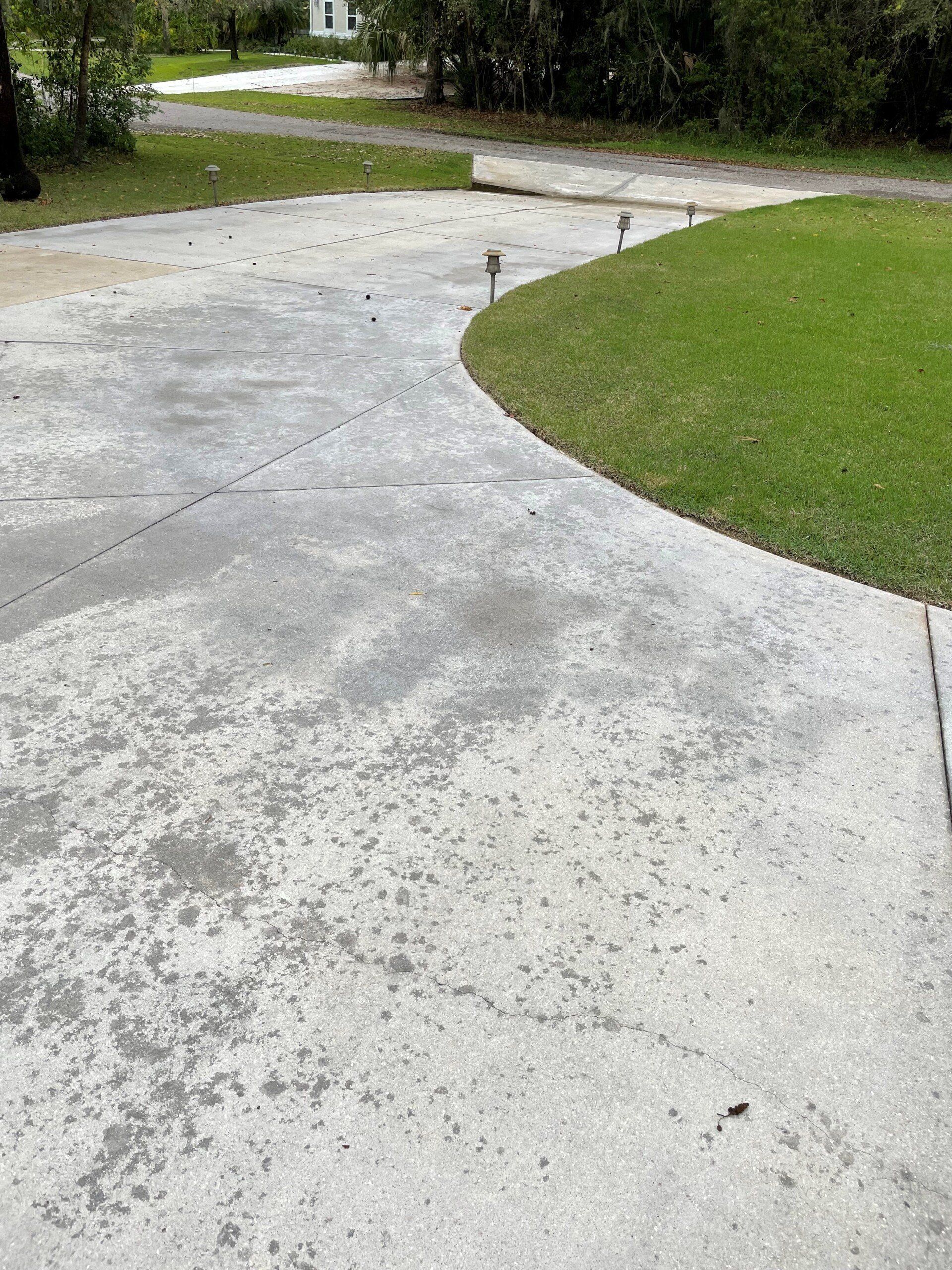 A paved concrete driveway curves toward a green lawn with small landscape lights lining the edge.