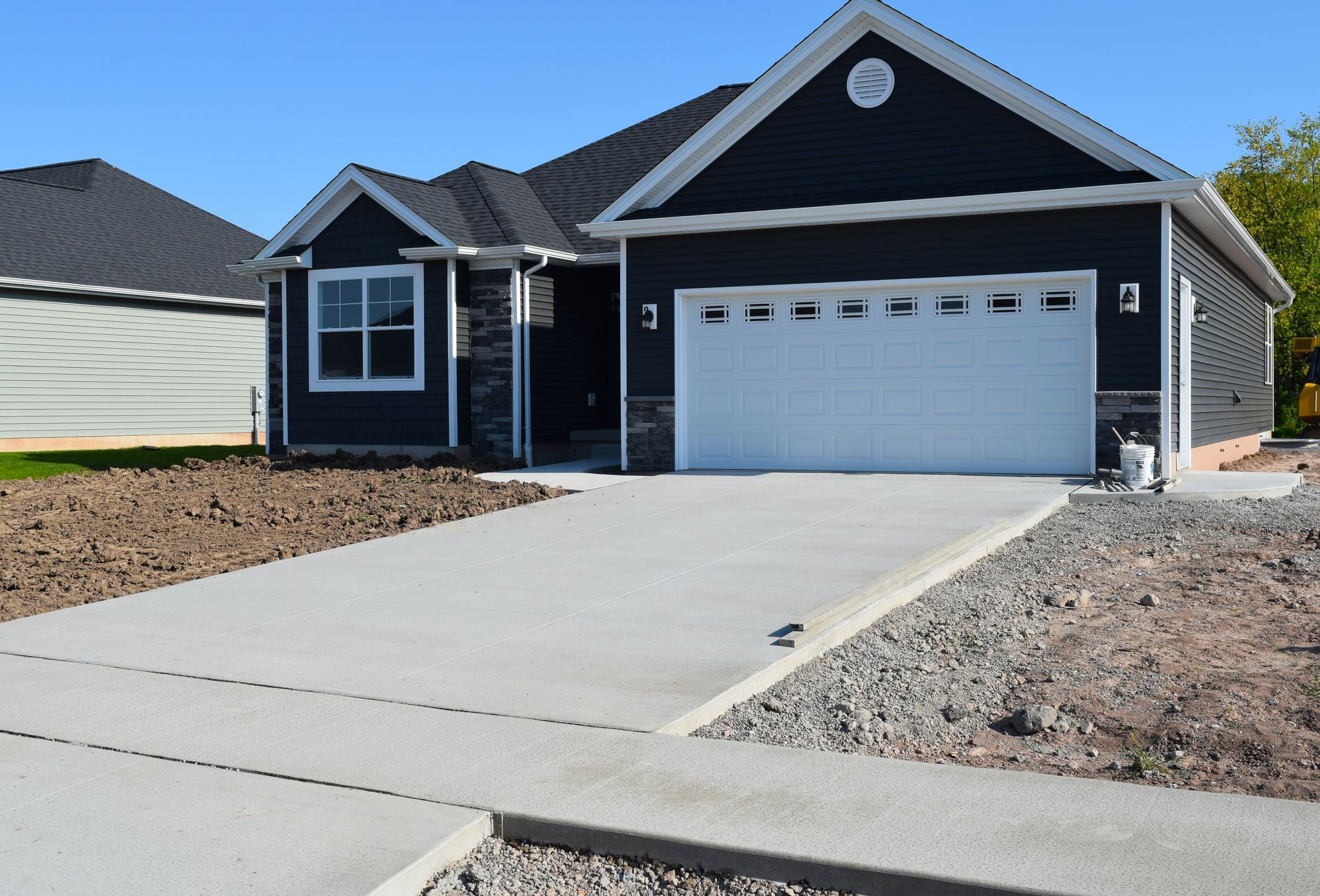 A new dark-sided house with a white garage door and a fresh concrete driveway under a clear blue sky.