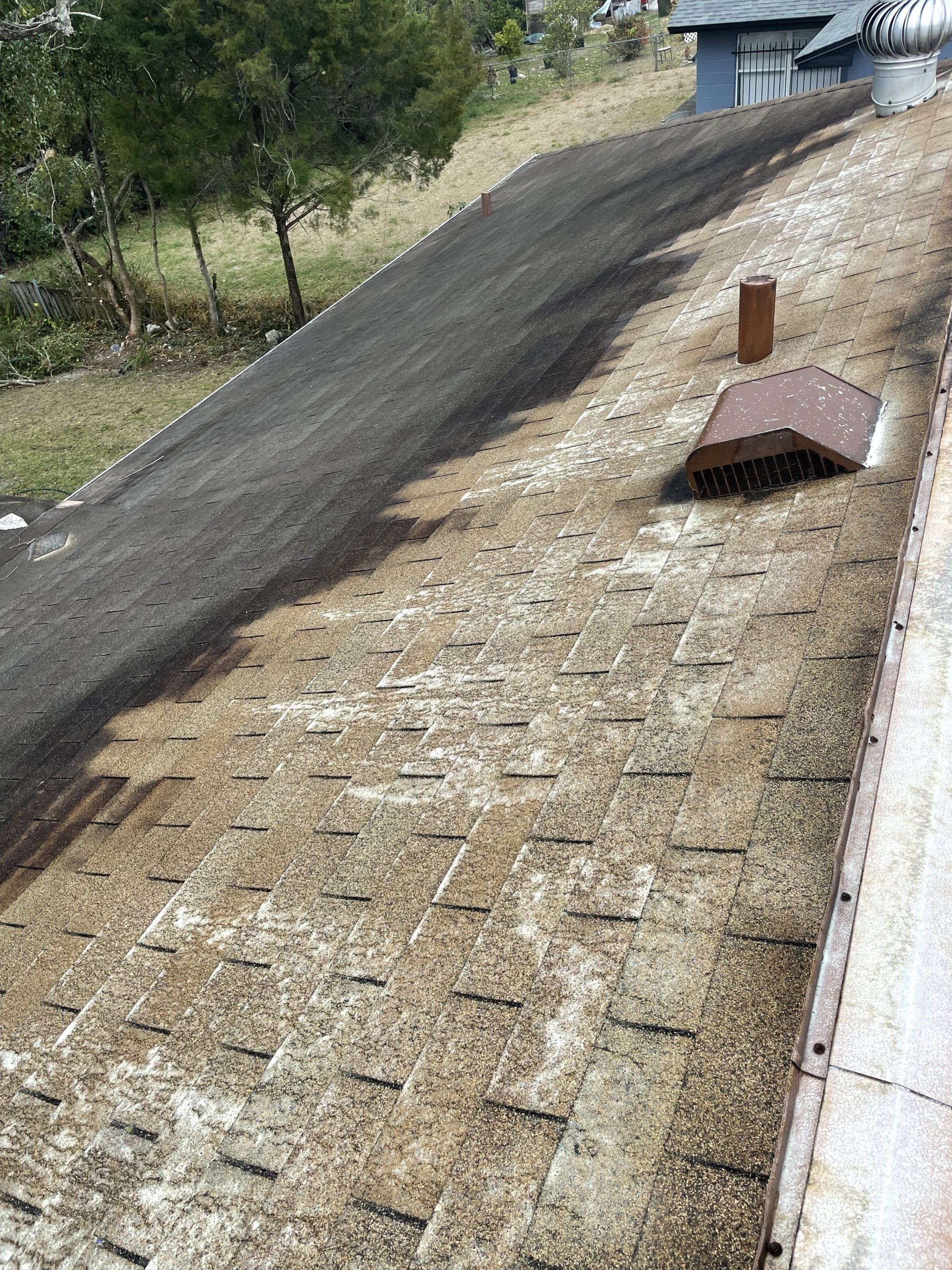 A weathered shingle roof features a dark stained section alongside lighter, worn shingles and a rectangular metal vent.