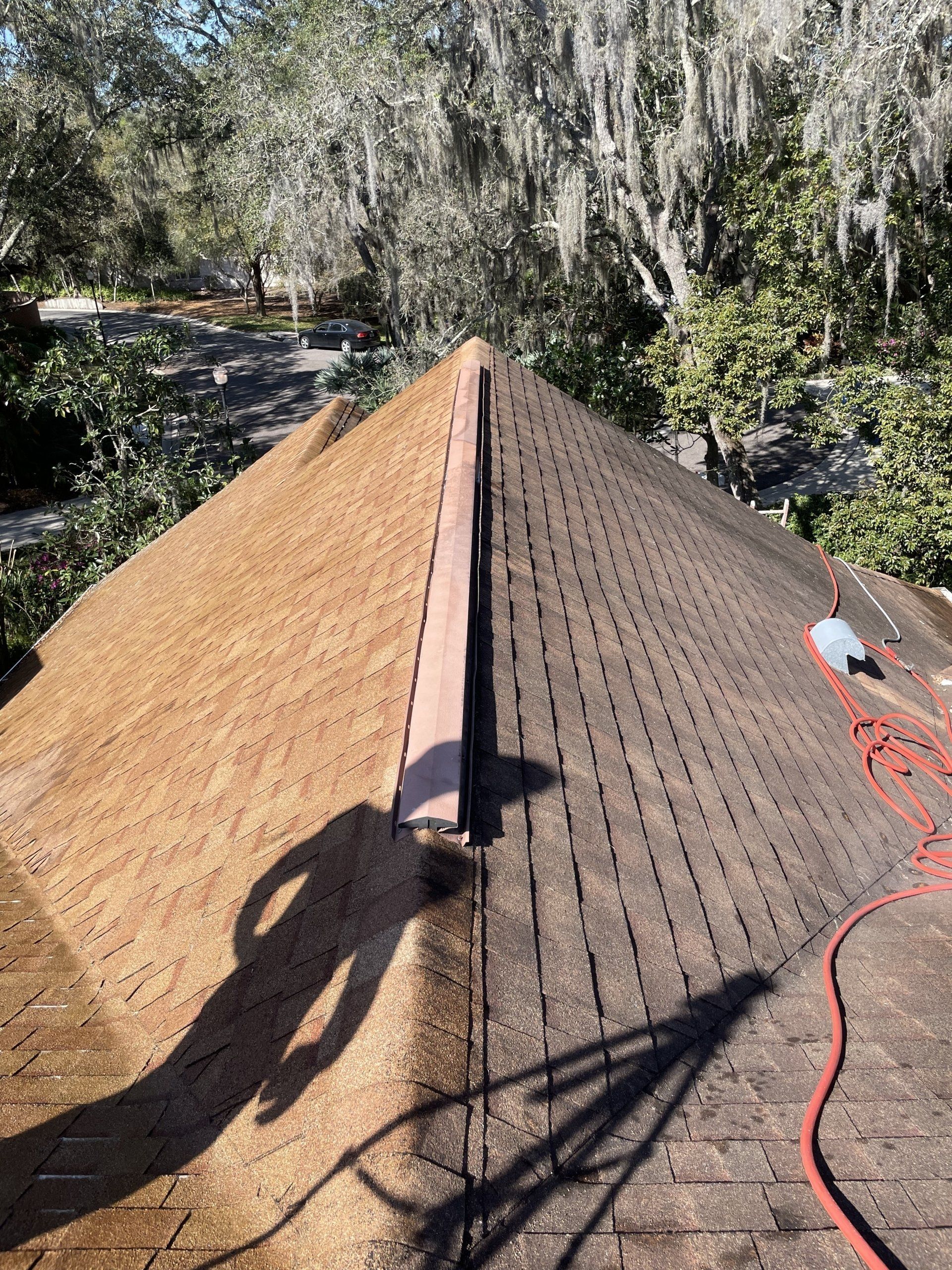 A high-angle view of a roof being repaired, showing two different shingle colors meeting at a ridge vent.