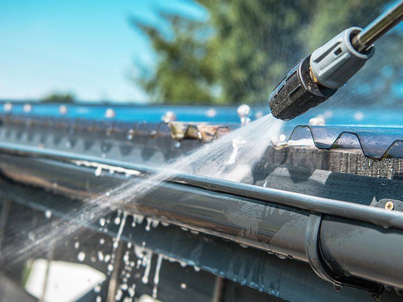 A pressure washer nozzle spraying water to clean a residential roof gutter.
