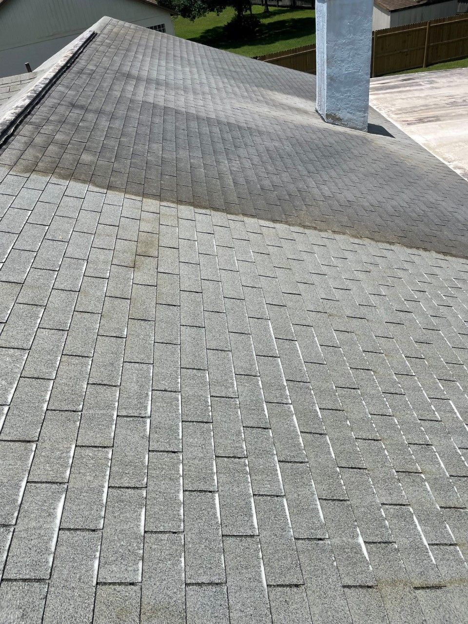 A high-angle view of a grey shingled roof with a chimney, showing a clear line of contrast from light to shadow.