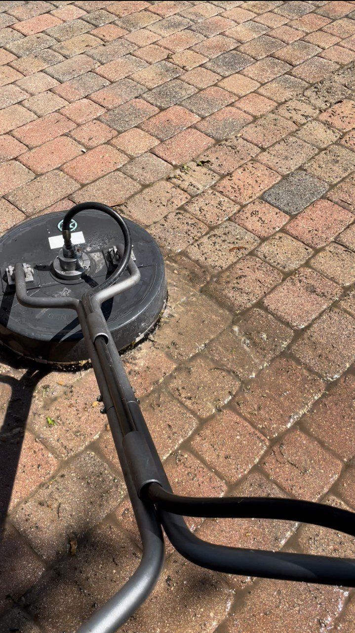 A surface cleaner power washing reddish-brown interlocking brick pavers on a sunny day.