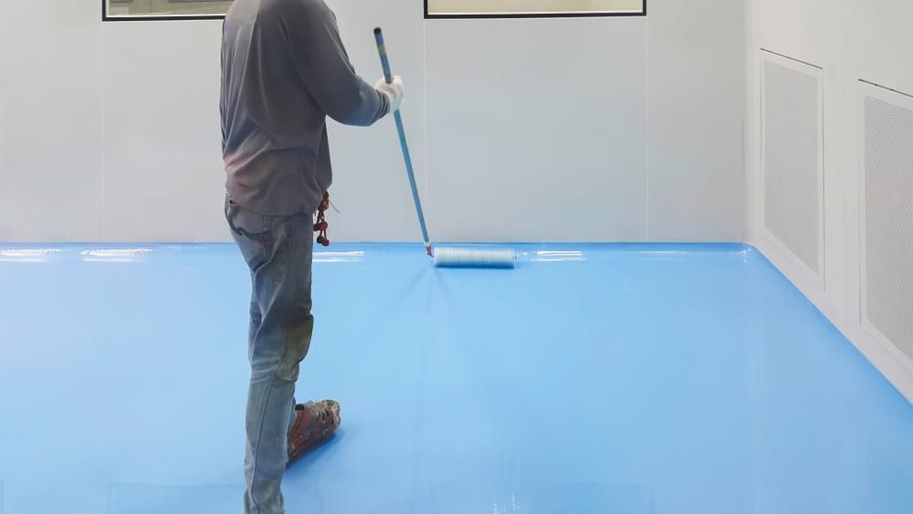 A Man Is Cleaning A Blue Floor With A Mop — B2B Flooring Solutions In Wauchope, NSW
