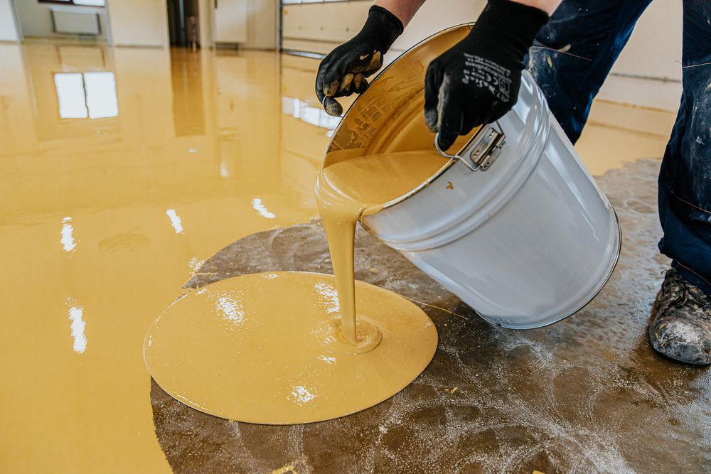 A Person Is Pouring Yellow Epoxy Into A Bucket — B2B Flooring Solutions In Kempsey, NSW