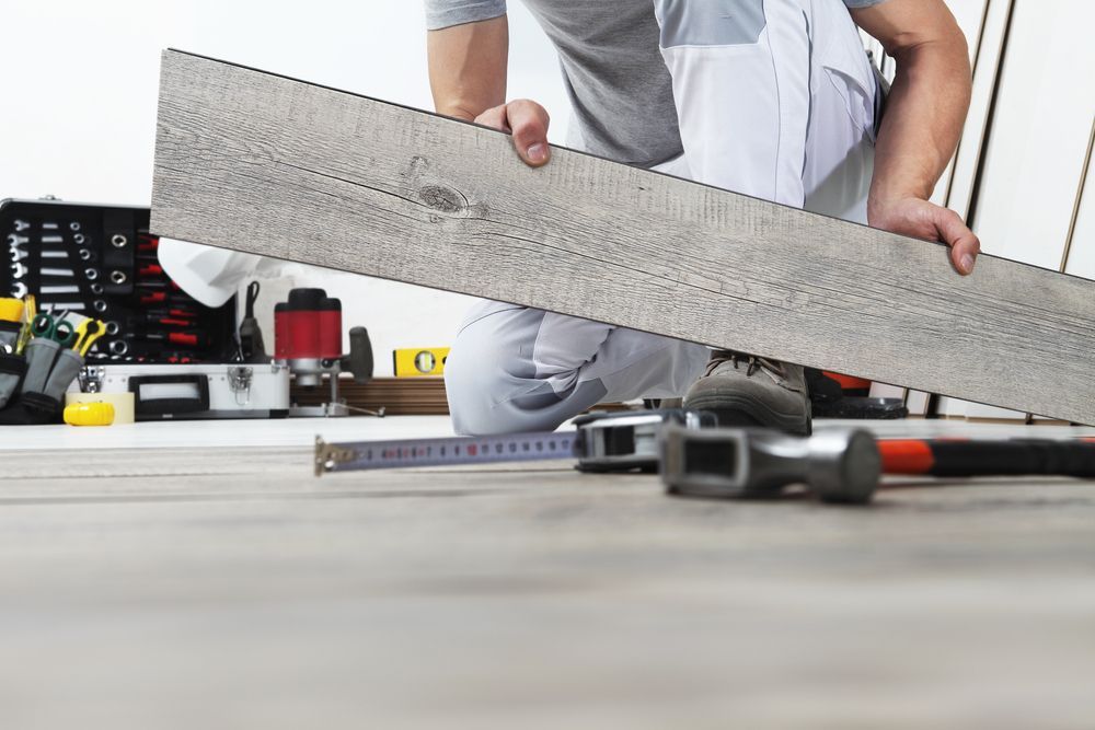 A Man Is Kneeling Down Holding A Piece Of Wood — B2B Flooring Solutions In Kempsey, NSW