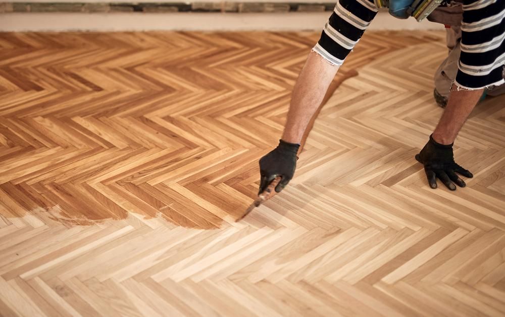 A Person Is Painting A Wooden Floor With A Brush — B2B Flooring Solutions In Clarence Valley, NSW