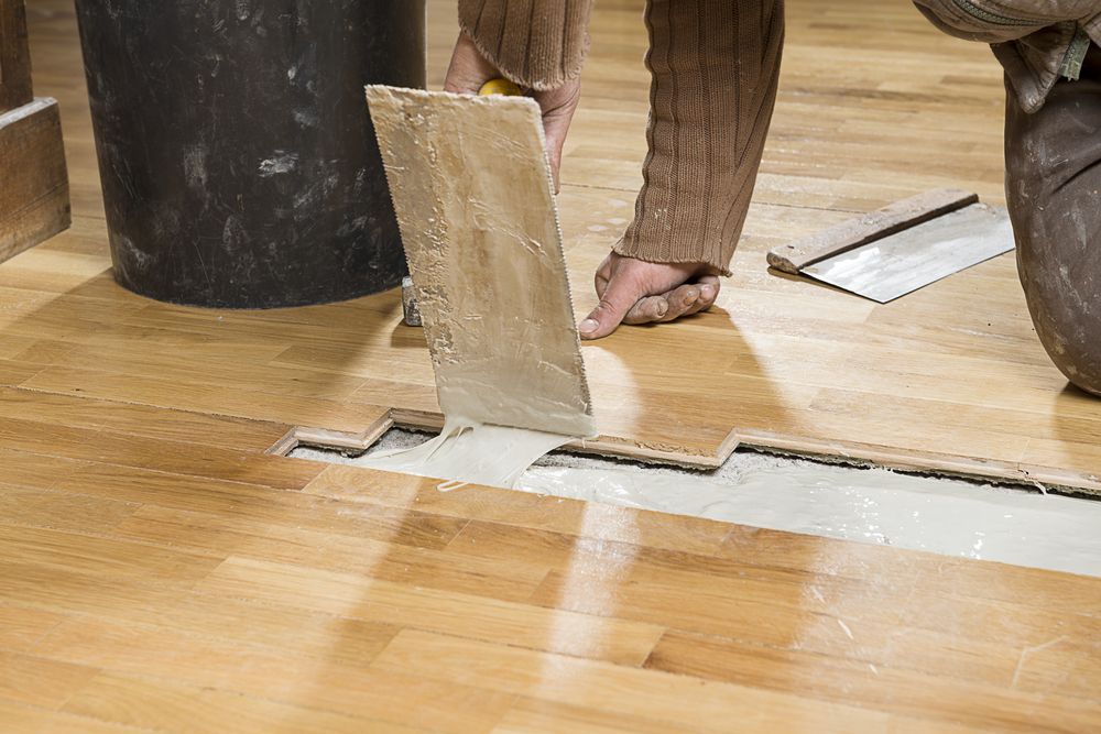 Skilled Carpenter Meticulously Applying Parquet Glue For B2b Flooring Solutions — B2B Flooring Solutions In Yamba, NSW