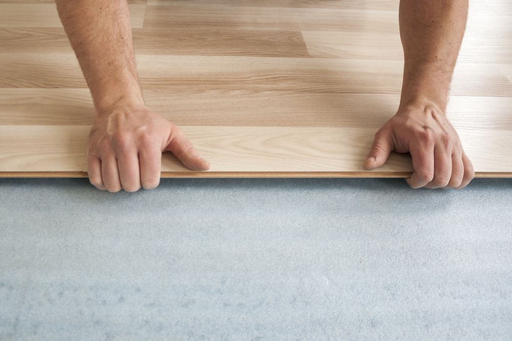 A Man Is Installing A Wooden Floor In A Room — B2B Flooring Solutions In Kempsey, NSW