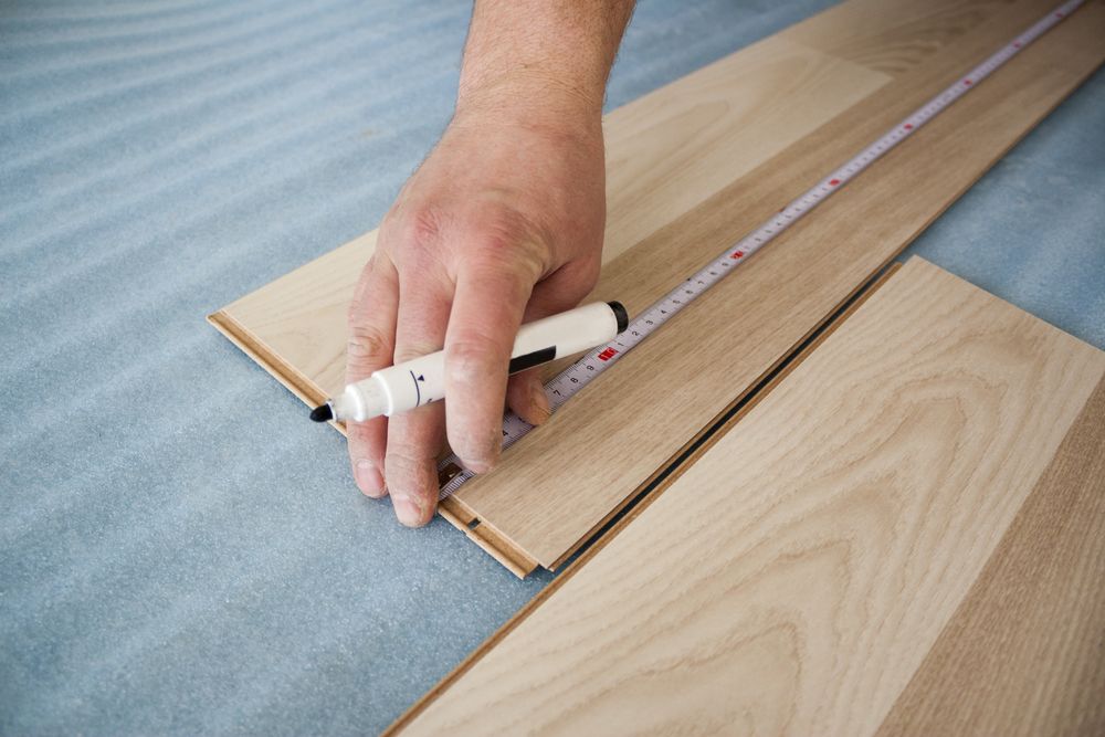 A Person Is Measuring A Piece Of Wood With A Tape Measure — B2B Flooring Solutions In Kempsey, NSW