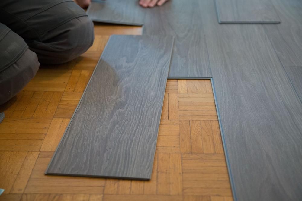 A Person Is Installing A Wooden Floor In A Room — B2B Flooring Solutions In Forster, NSW