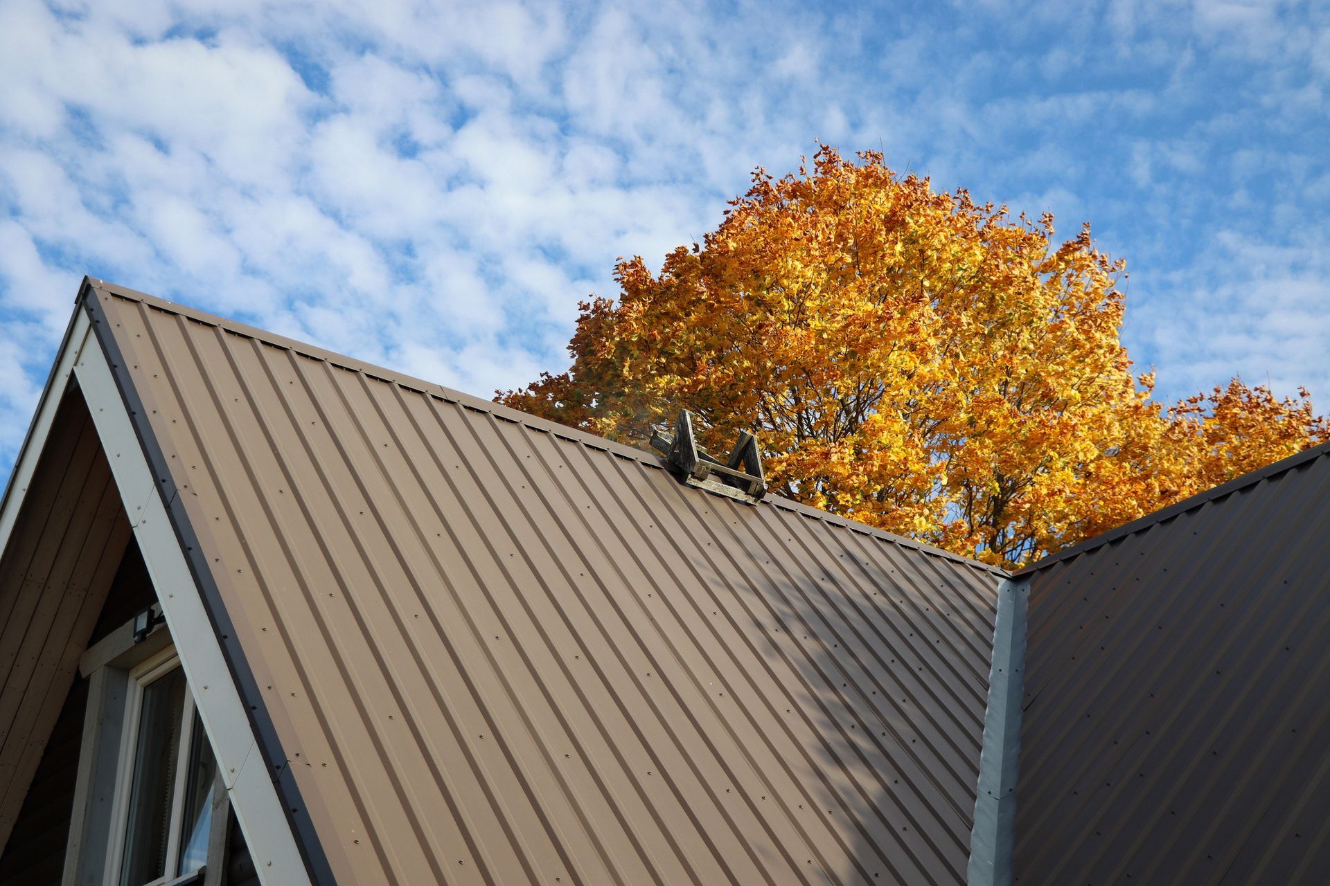 A brown roof of a house with a tree in the background.