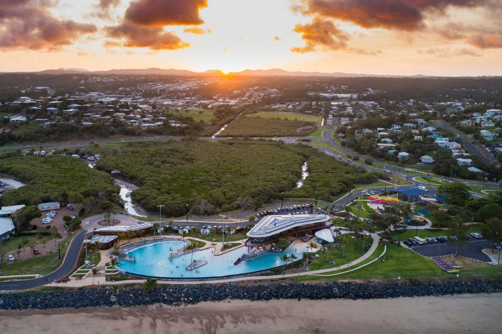 Aerial view of a coastal city at sunset, with a large lagoon, buildings, and green space — HYVIS Plant Hire Pty Ltd in Mulambin, QLD