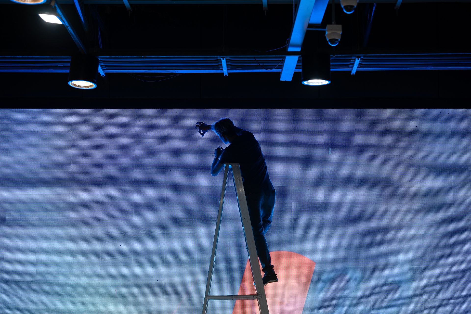 A Person Climbs a Ladder, Adjusting Equipment in Front of a Blue Screen — HYVIS Plant Hire Pty Ltd in Yeppoon, QLD