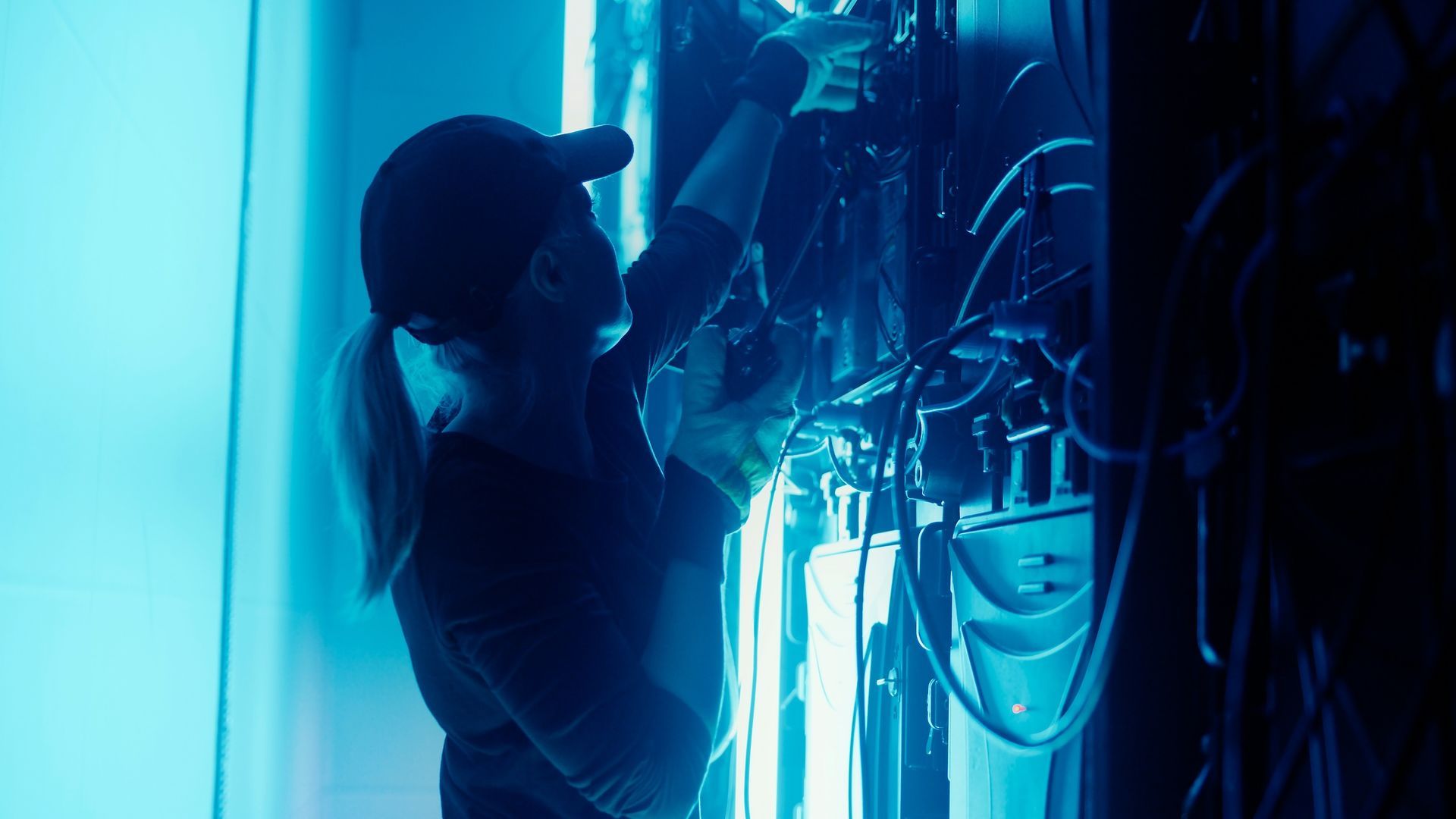 Woman In Cap Works On Wires In Blue-lit Room — HYVIS Plant Hire Pty Ltd in Mulambin, QLD