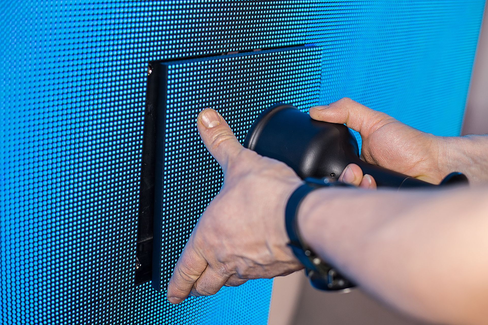 Person using a tool to adjust a black bracket on a blue, pixelated display — HYVIS Plant Hire Pty Ltd in Mulambin, QLD