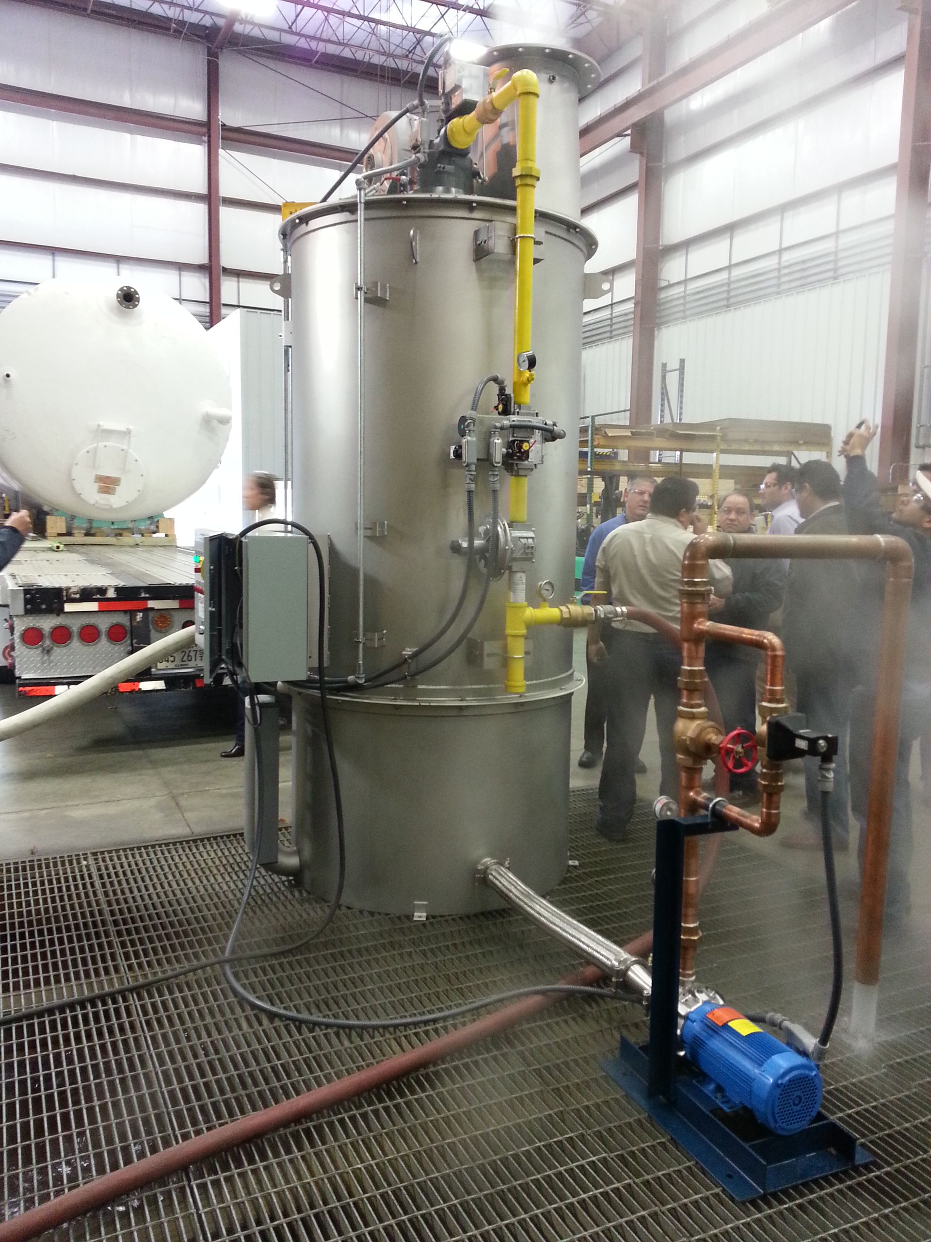 Un grupo de personas está de pie alrededor de un gran tanque de acero inoxidable.