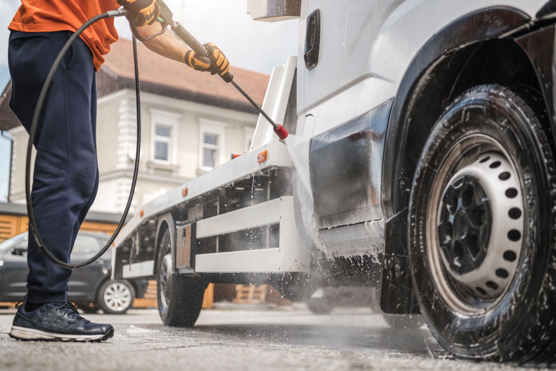 A person washing a white tow truck with a pressure washer.