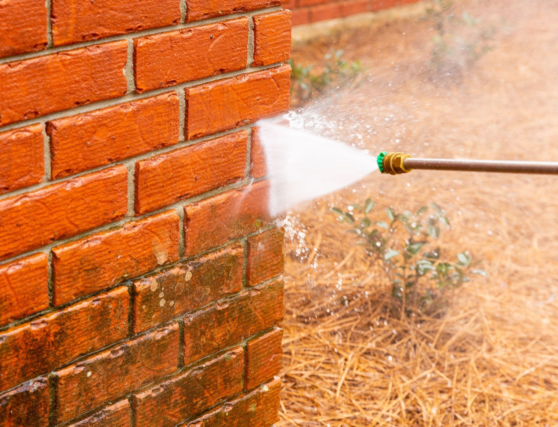Pressure washer spraying water onto a brick wall, cleaning away green stains.