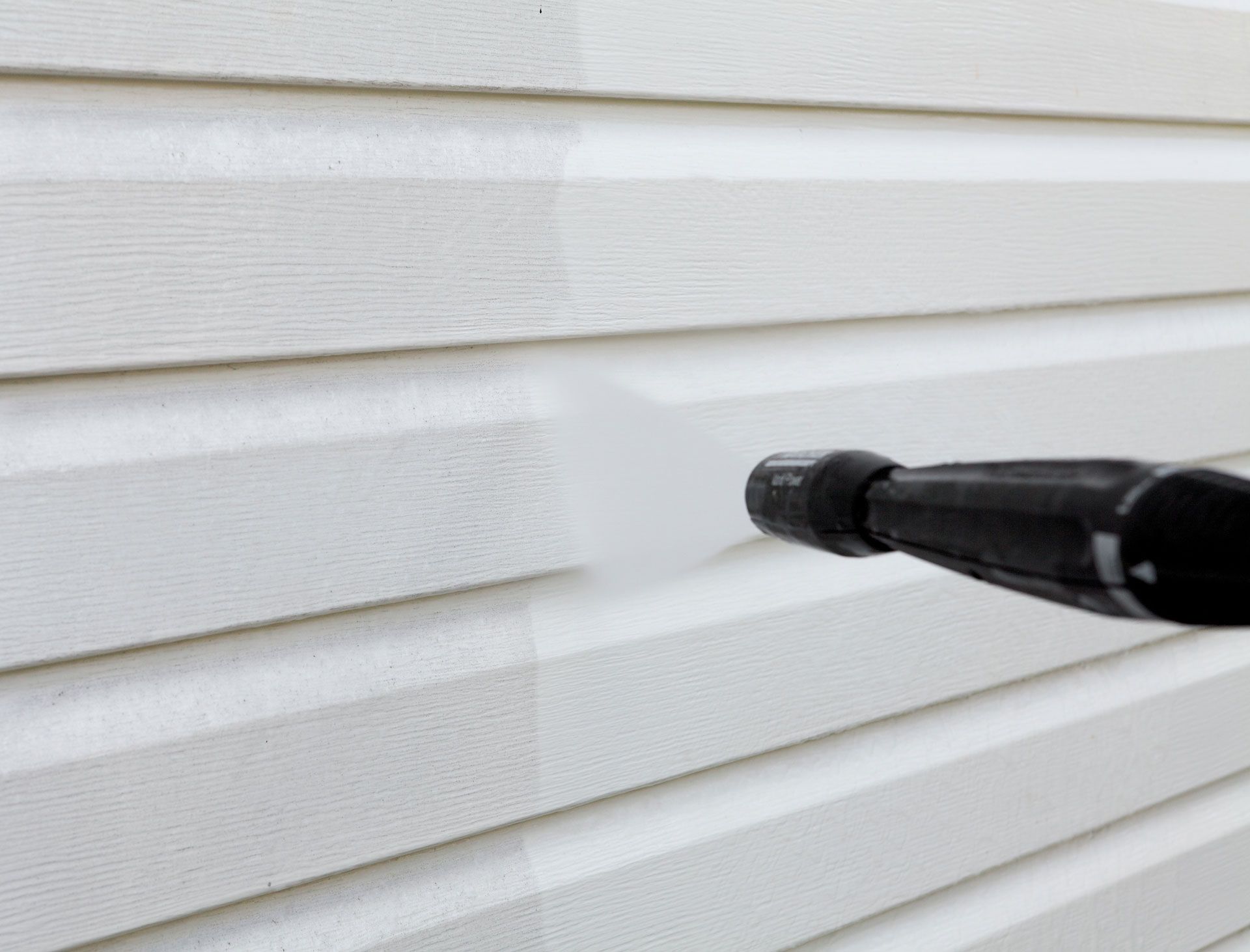 Pressure washer cleaning white siding, revealing a cleaner section.