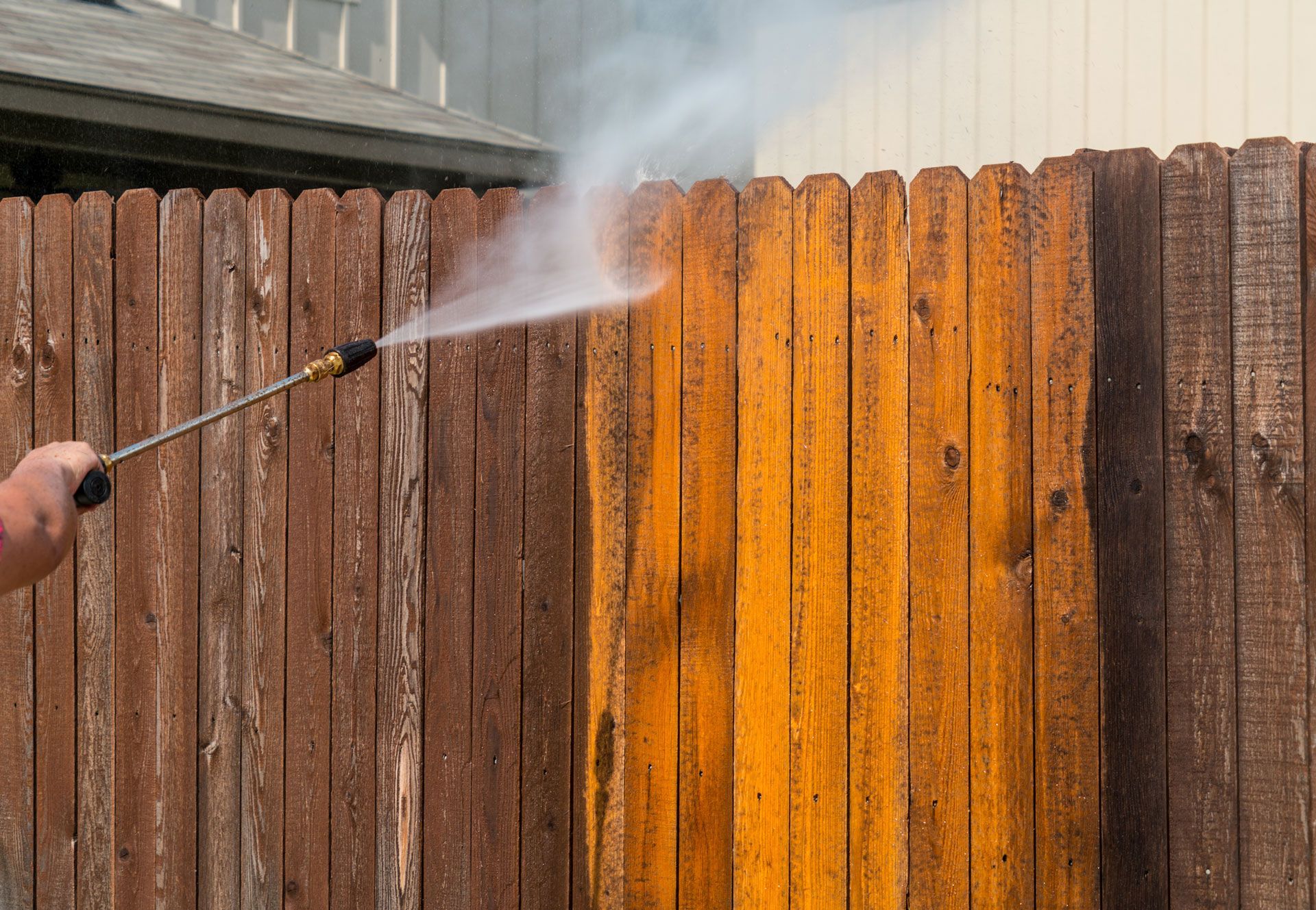 Pressure washing a wooden fence, revealing cleaner, lighter wood.
