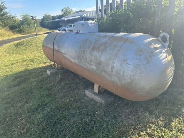 Large, horizontal metal propane tank on concrete blocks in a grassy outdoor setting.
