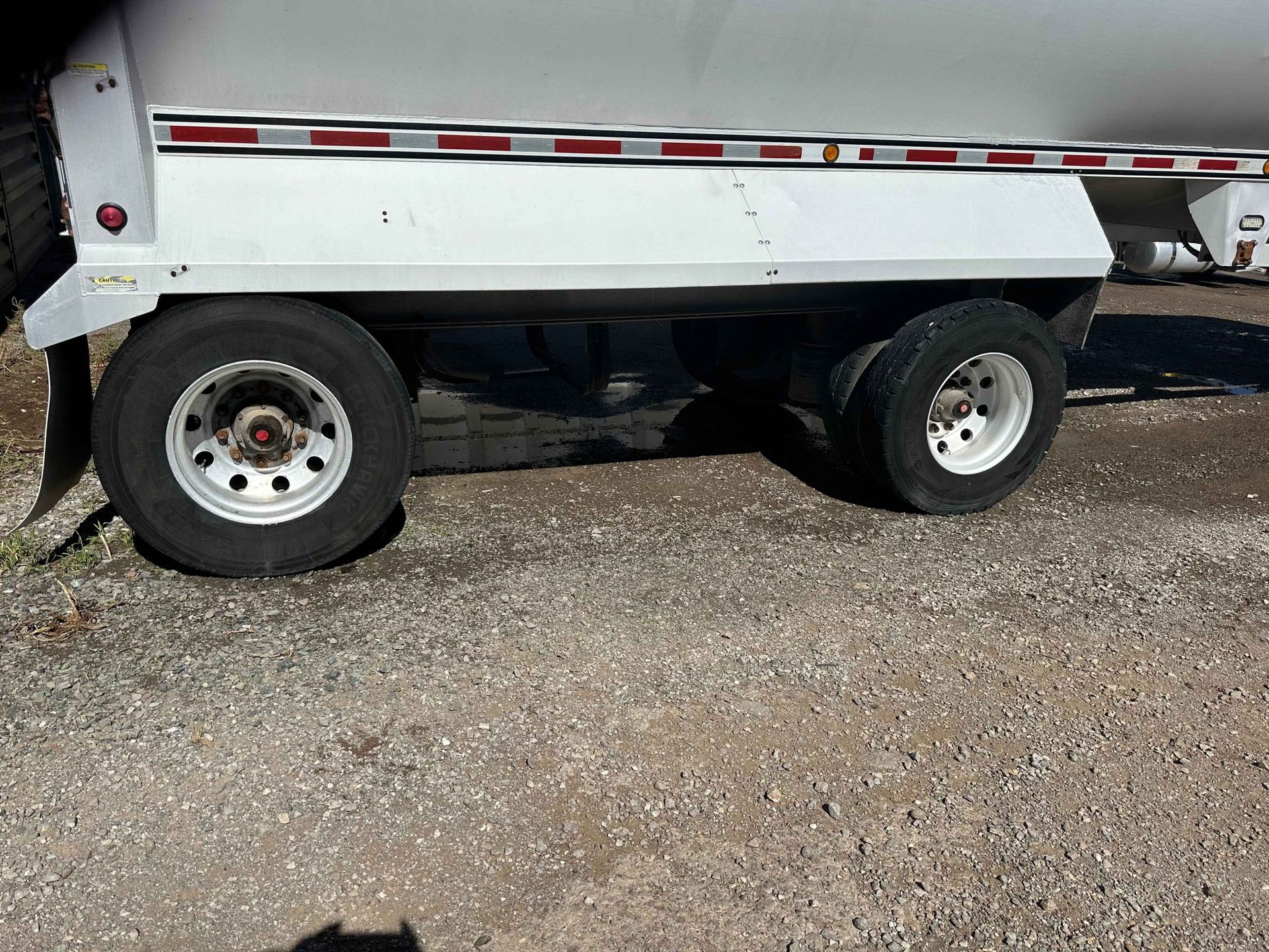 White trailer with two wheels on gravel.