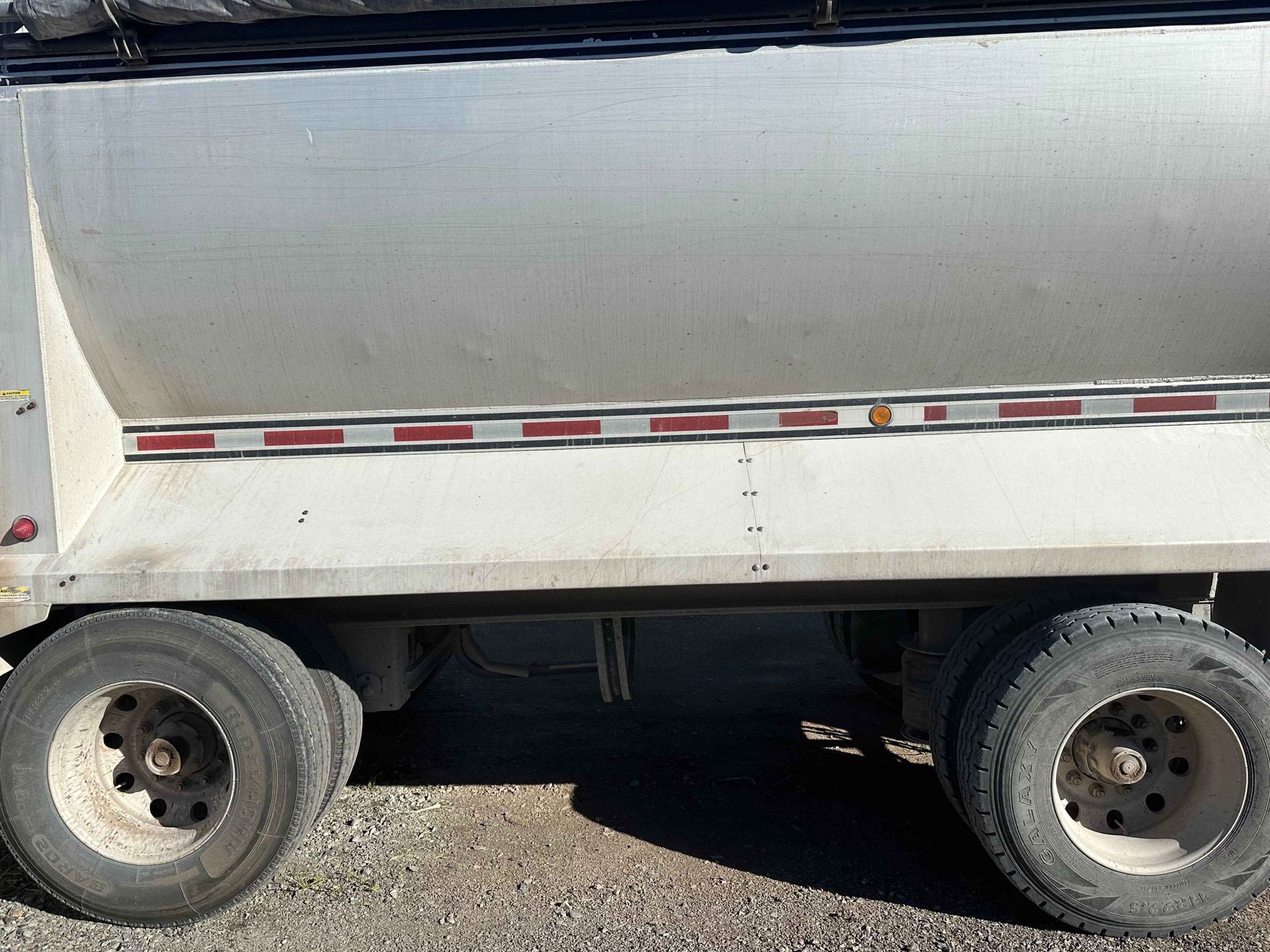 Side view of a silver dump truck trailer with visible tires and reflective tape.