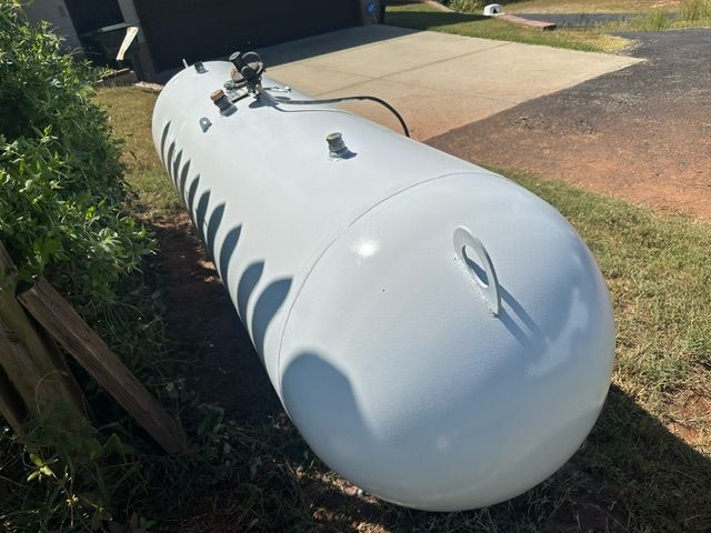 White propane tank lying on a grassy area, near a driveway and garage.