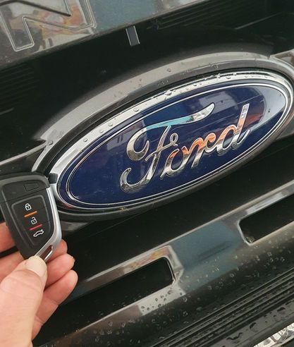 A person is holding a remote control in front of a ford logo.