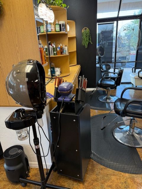 Hair salon interior with styling chairs, dryer, and products on shelves.