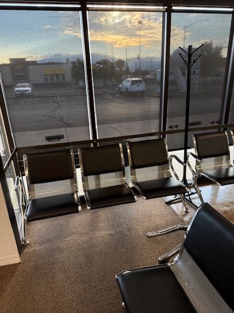 Airport waiting area with metal chairs and a window view of vehicles and mountains.