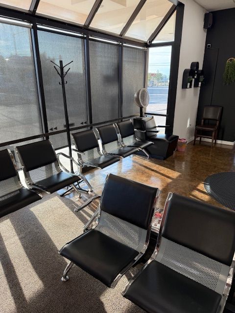 Waiting area with black chairs, coat rack, and window blinds.