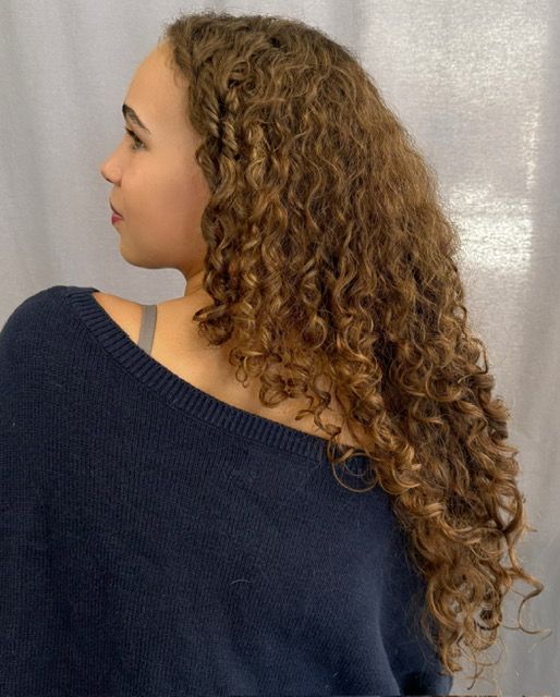 Woman with long, curly brown hair, turned to the side, wearing a navy sweater.