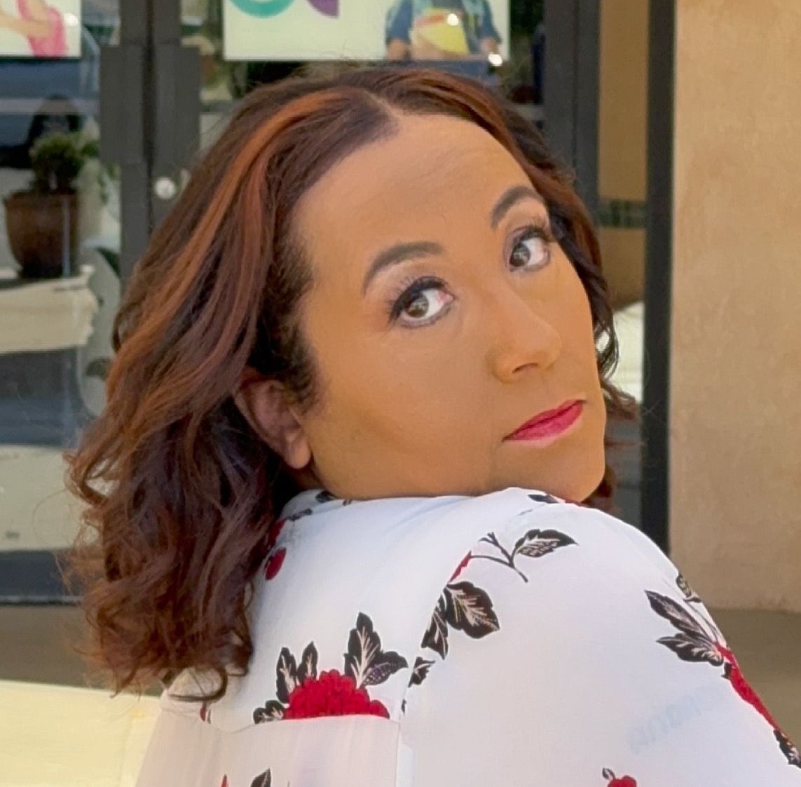Woman with brown hair, looking over her shoulder, wearing a floral top.