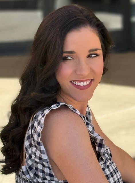 Woman with long, wavy dark hair, wearing a black and white checkered dress, smiles and looks to the side.