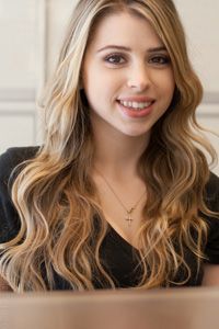 Blonde-haired woman smiling, wearing a black top and a small necklace.
