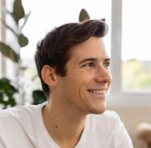 A young man in a white shirt is smiling while sitting on a couch.