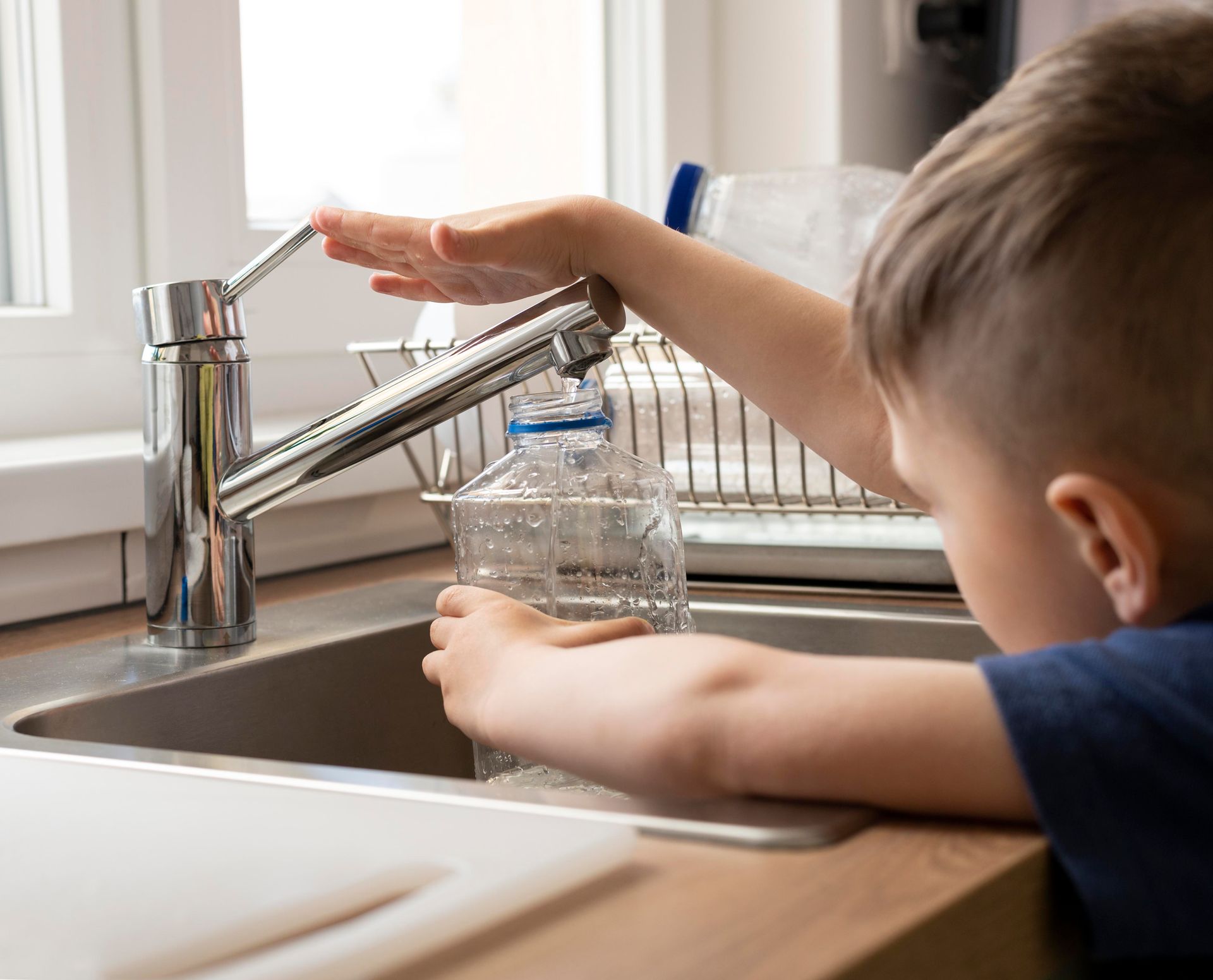 A young boy is washing his hands in a kitchen sink.